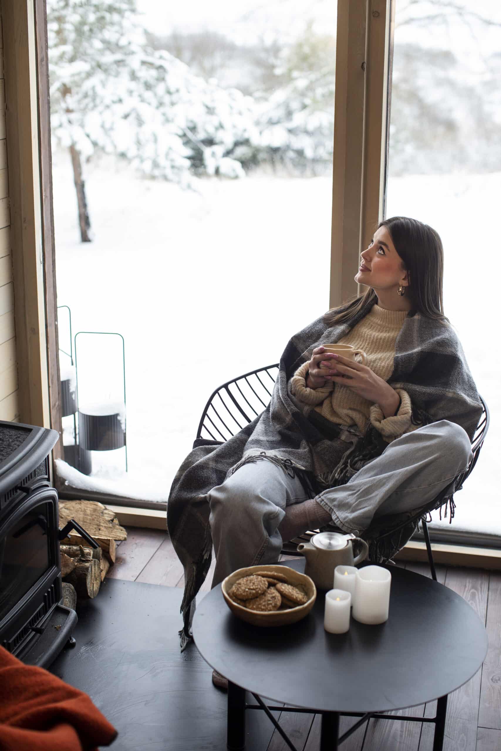 Mujer mirando por la ventana de su casa, reflexionando en invierno